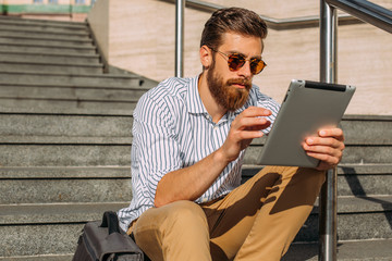 Young Caucasian businessman using a digital tablet in front of a corporate building.