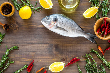Mediterranian cuisine. Dorado with rosemary, pepper, chili, lemon on wooden background top view copyspace