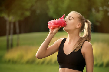Sporty young woman drinking protein shake outdoors