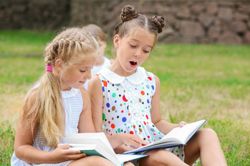 Cute little girls reading books in park