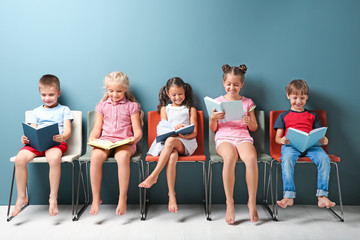 Cute little children reading books while sitting near color wall