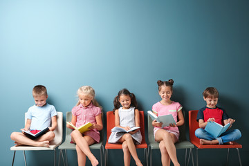 Cute little children reading books while sitting near color wall