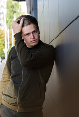 Portrait serious young man leaning against grey wall. Handsome young man on grey background looking at camera. Model