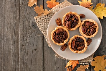 Plate of mini pecan pie tarts, rustic overhead table scene on a wood background