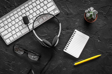 Workspace at call center. Headphones and notebook near keyboard on black background top view