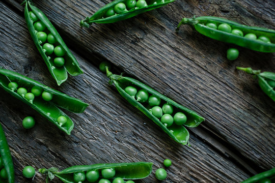 Open garden pea pods on a wood surface.