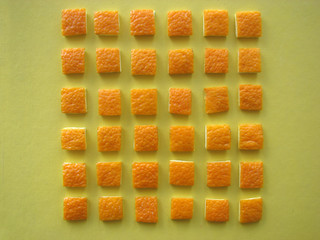 Texture of the squares cut from the orange peel on a yellow background.
