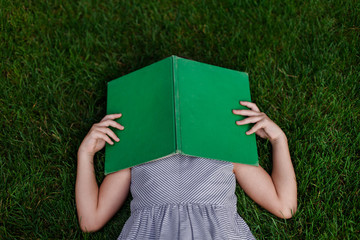 School girl laying in grass with a green, vintage book over her head