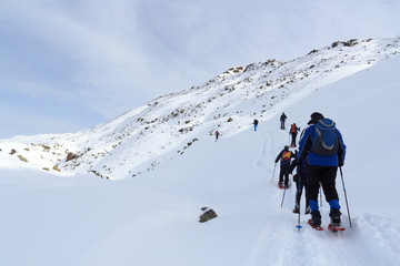 Group of people hiking on snowshoes and mountain snow panorama with blue sky in Stubai Alps, Austria