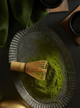 Green matcha powder with bamboo whisk on pewter plate