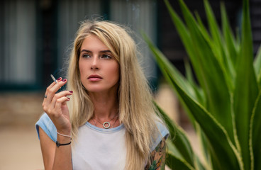 Beautiful blonde girl smokes a cigarette. Women's hands with a tattoo. Urban fashion