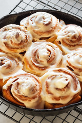 Close Up on Iced Cinnamon Buns or Rolls in Cast Iron Skillet on Cooling Rack