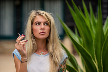 Beautiful blonde girl smokes a cigarette. Women's hands with a tattoo. Urban fashion