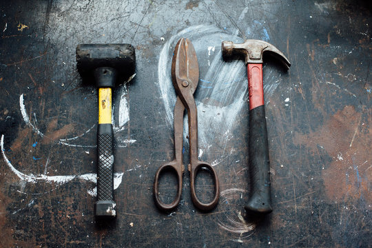 A mallet, tin nippers or wire cutters and hammer on a worn work table.