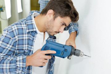 male builder drilling holes in wall at construction site