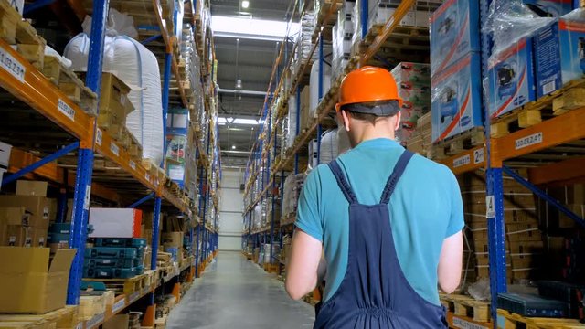 A back view on a warehouse employee walking an aisle at a storage. 4K.