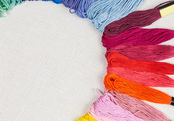 skeins of multicolored embroidery threads on white cotton canvas