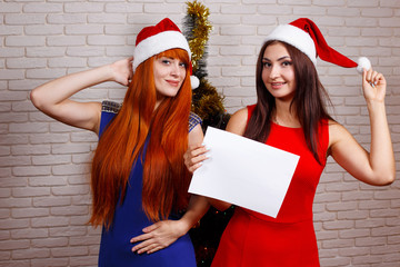 Two beautiful smiling women in Santa caps with empty board in hands. Free space for advertisement...
