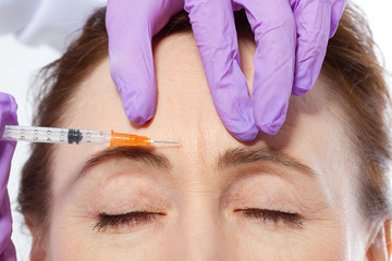 Forehead of middle age woman and doctor giving injection