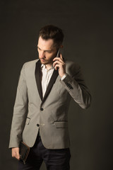 portrait of a young man talking on the phone with an unshaven face on a suit with a pensive face on a dark background