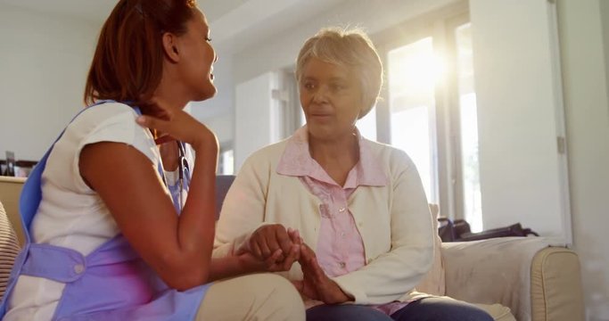 Mixed-race woman doctor comforting senior woman in living room 