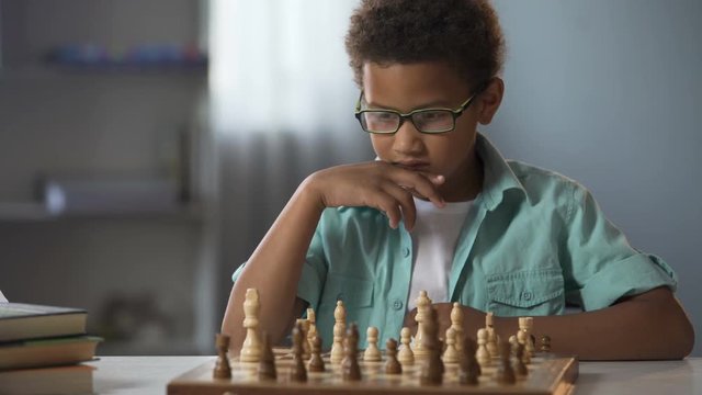 African American boy logically thinking out strategy of playing chess, hobby
