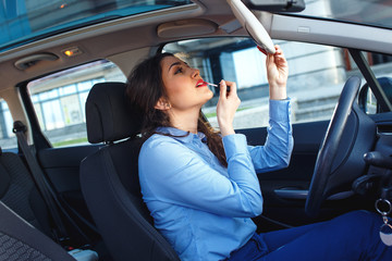 Beautiful young business woman sitting in the car and apply make up.