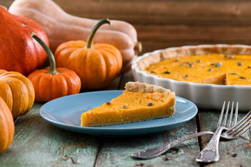 Homemade delicious pumpkin pie with pumpkin seeds on blue plate with bright orange pumpkins on background