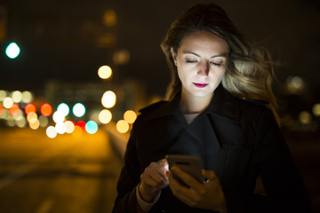 young handsom caucasian woman holding a smartphone on the dark city