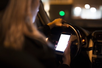 Pretty young woman using her smart phone while driving her car at night