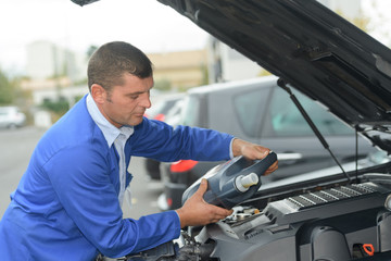 car mechanic replacing and pouring fresh oil into engine