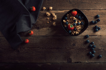 Cereal bowl with fresh fruits on dark old wood table top. Healthy breakfast ingredients with granola and berries. Top view.
