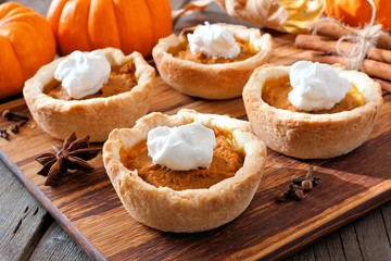 Mini pumpkin pie tarts, close up scene on a wooden server against a rustic wood background