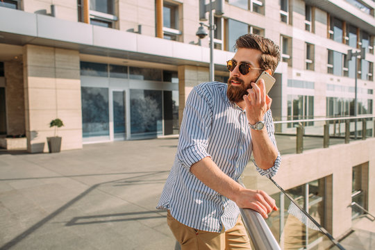 Young Caucasian businessman using phone in front of a corporate building.