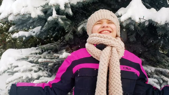 4k footage of happy laughing girl standing under snow falling from pine tree
