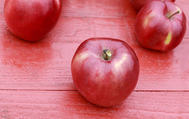 ripe red apples lie on a wooden table on colorful maple leaves in autumn garden
