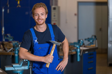 Metal worker posing in workshop with hammer in his hand