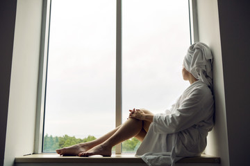 girl in a Bathrobe and towel on head sits on the window