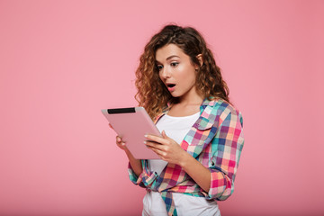 Young caucasian brunette lady using tablet computer isolated over pink