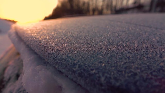 SLOW MOTION CLOSE UP DOF: Beautiful morning frost on frozen car at golden sunrise. Sparkling hoarfrost on frozen car roof and windshield. Icy snowflakes on frosty car glittering in cold morning sun. 