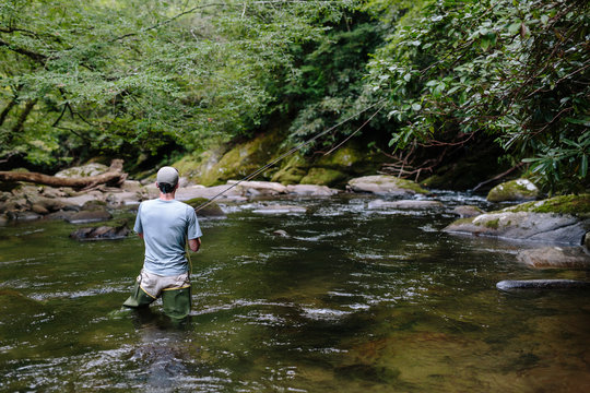 Man fly-fishing in clear river trying to catch fish