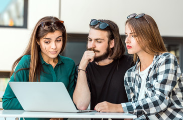 Group of students wear glasses have work conversation outdoor cafe, table with tablet computer before modern building wall, sunny day