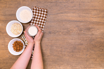Plant alternative milk recipe: almond, oat, rice in woman hands on the wood background