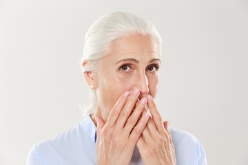 Close-up portrait of charming old lady, covering her mouth with hands, looking at camera