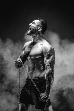 Side view of shirtless muscular man screaming and holding chain.