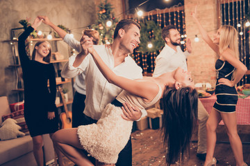 Excited, welldressed, cheerful, elegant husband holds cute wife, lean, she bending over, raised up leg, group of festive fancy luxury classy models with hot figures realx, enjoy, funky night - obrazy, fototapety, plakaty