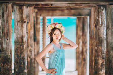 A young woman wearing a dress is standing on the beach under a pier