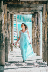 A young woman wearing a dress is standing on the beach under a pier