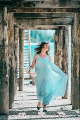 A young woman wearing a dress is standing on the beach under a pier