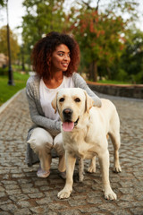 Young smiling lady in casual clothes sitting and hugging dog in park
